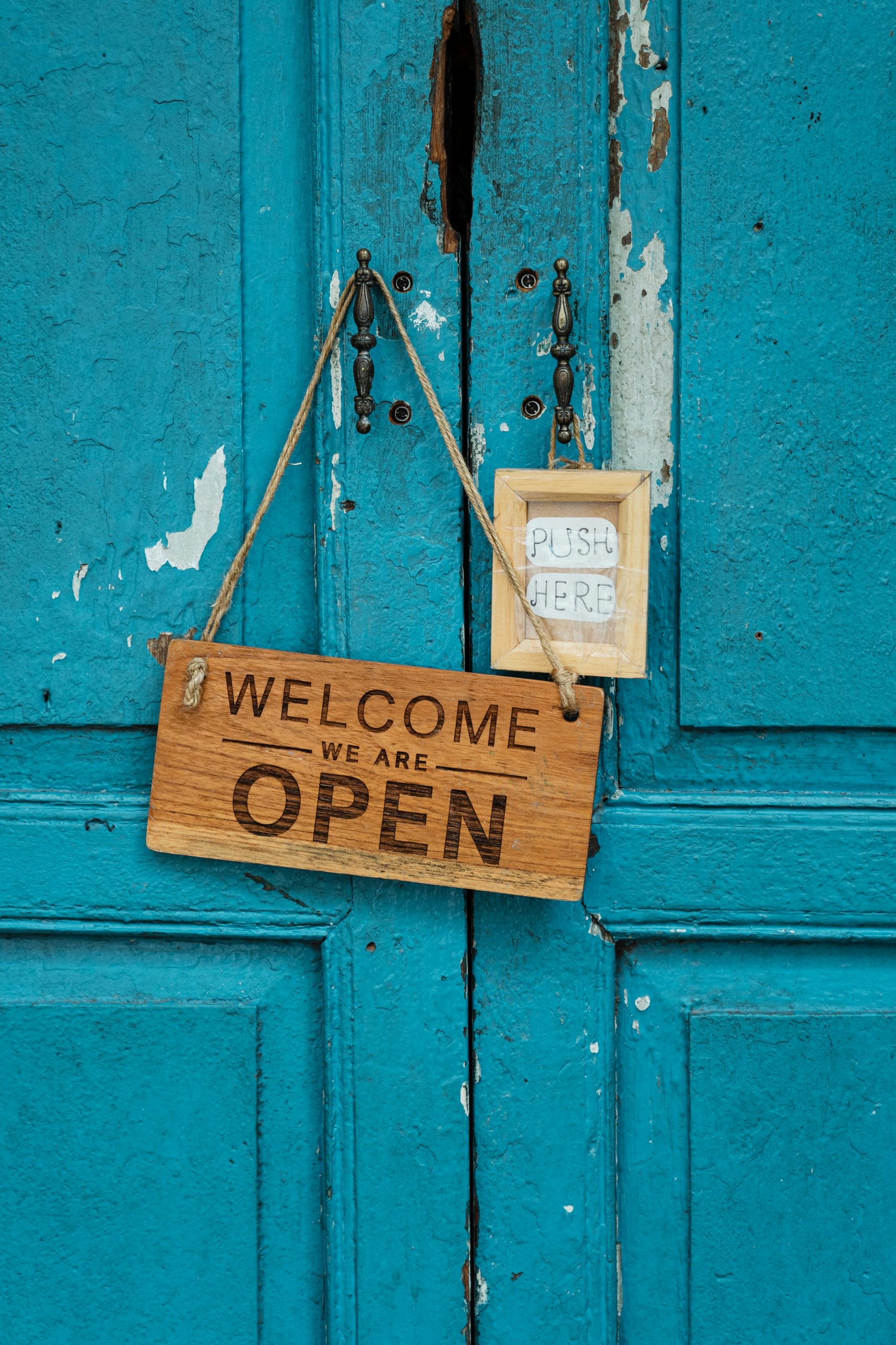 Graviertes Holzschild mit Aufschrift Welcome We Are Open an einer rustikalen Eingangstür