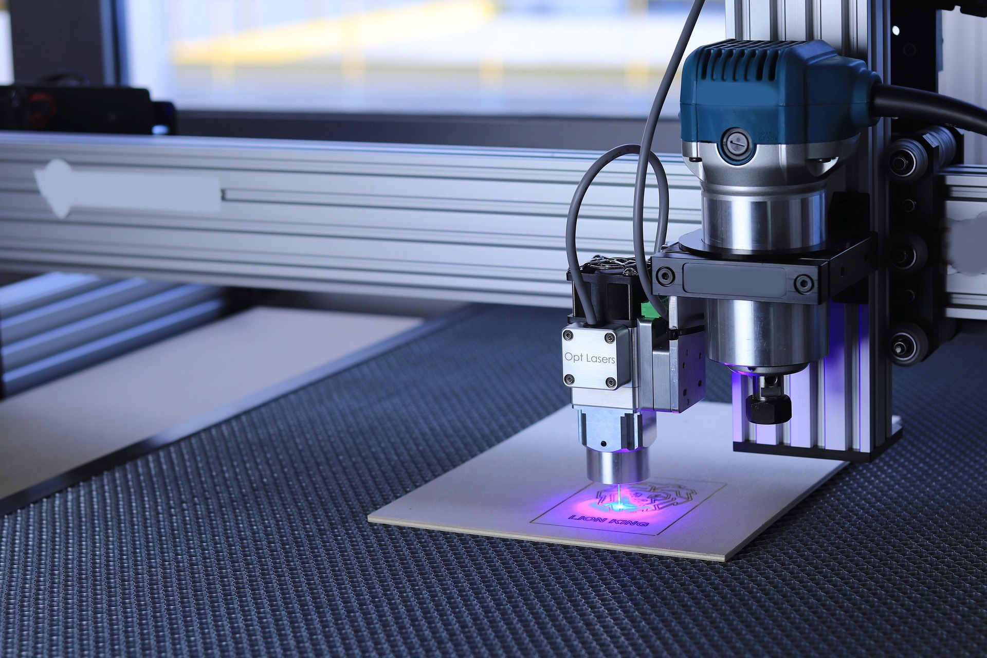 Lasergravurmaschine mit blauem Laserstrahl graviert ein Motiv auf Holzplatte