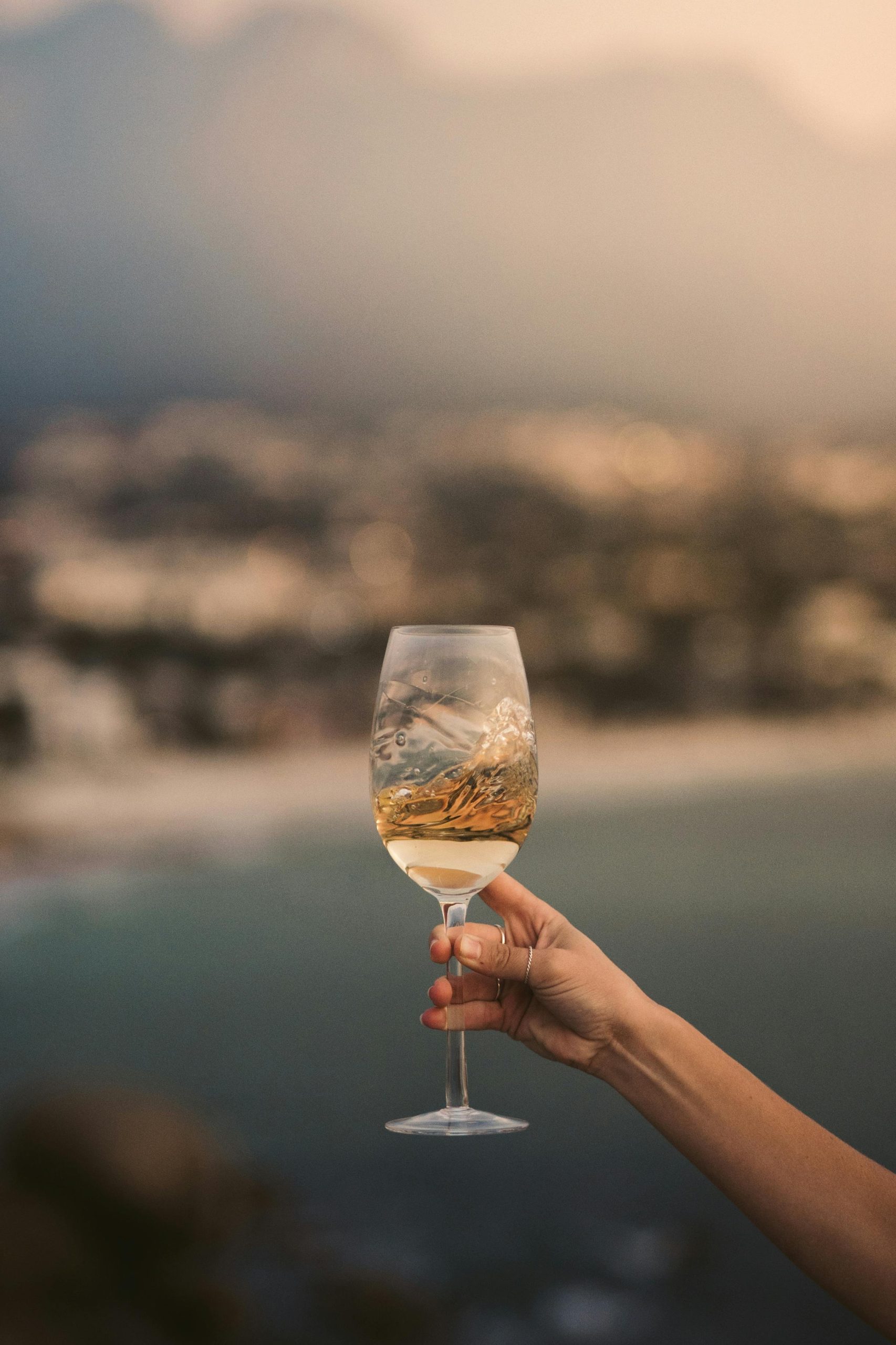 Hand hält ein elegantes Weinglas mit Weißwein vor verschwommenem Naturhintergrund
